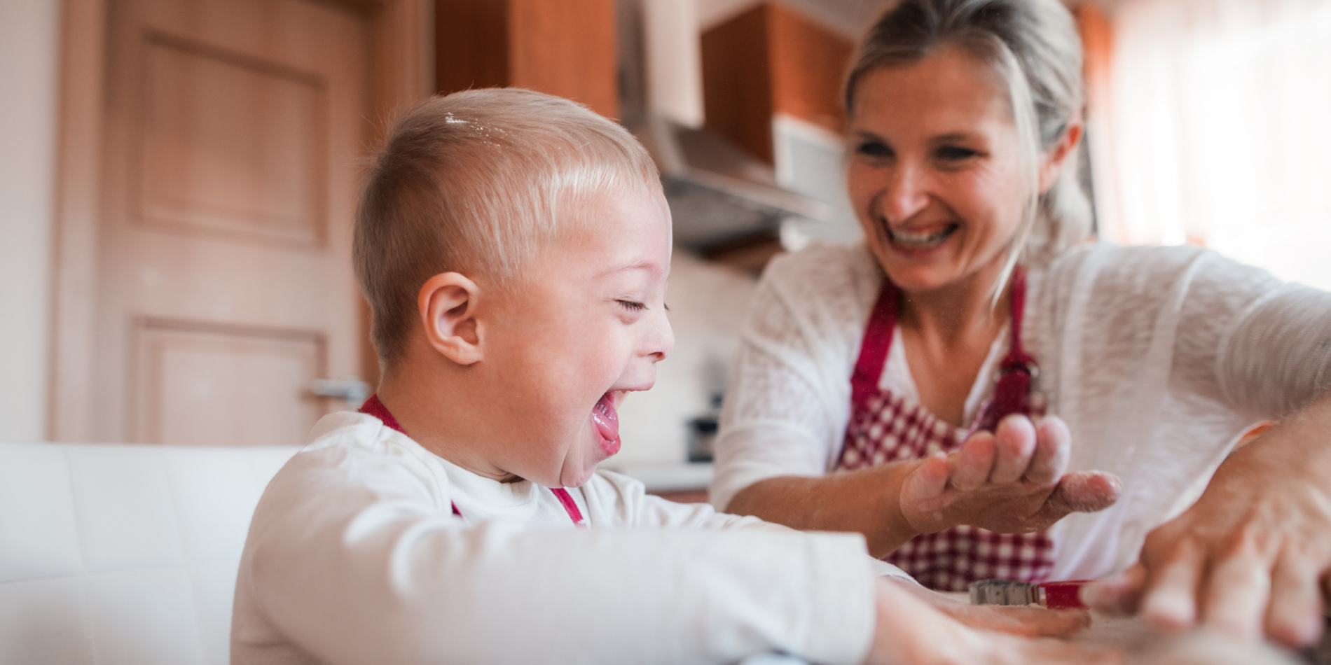A laughing handicapped down syndrome child with his mother indoors baking