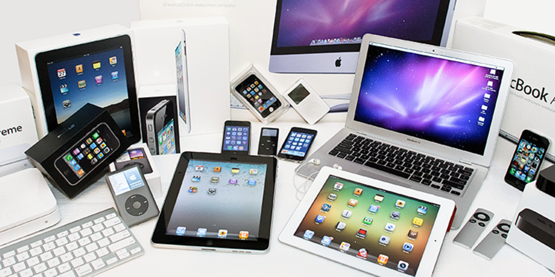 Various Apple products displayed on table: tablets, laptops, phones, etc.