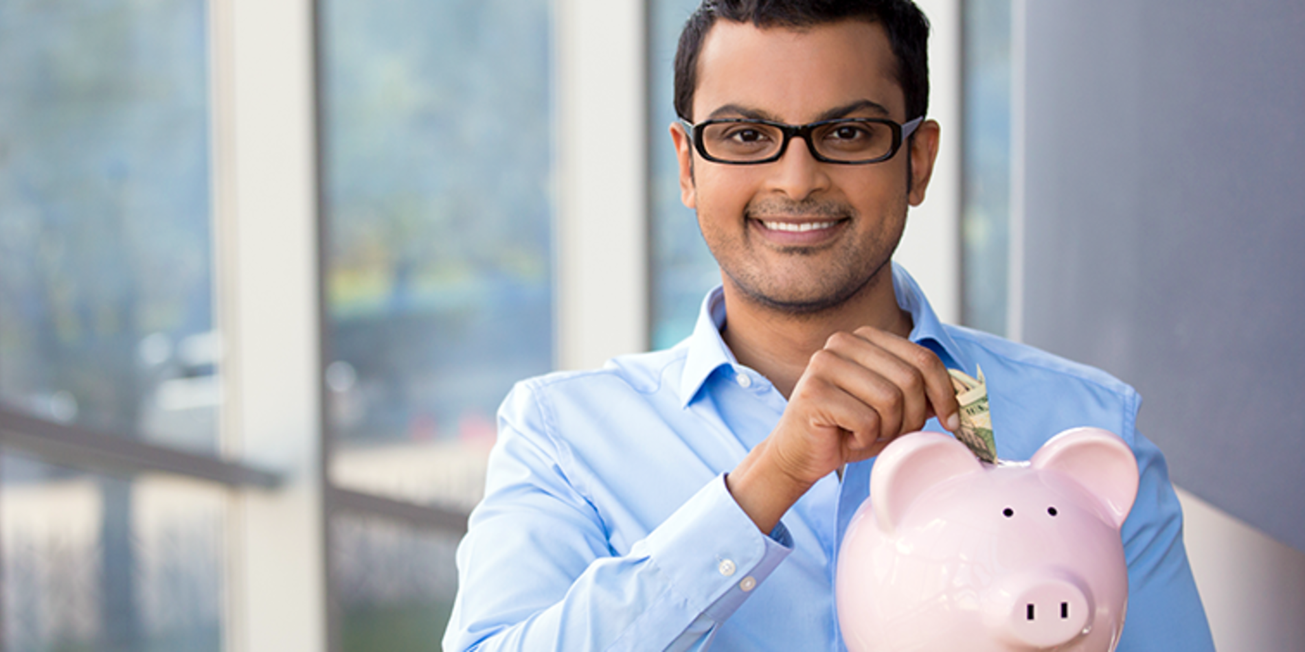 Male student wearing glasses withdrawing money from piggy bank