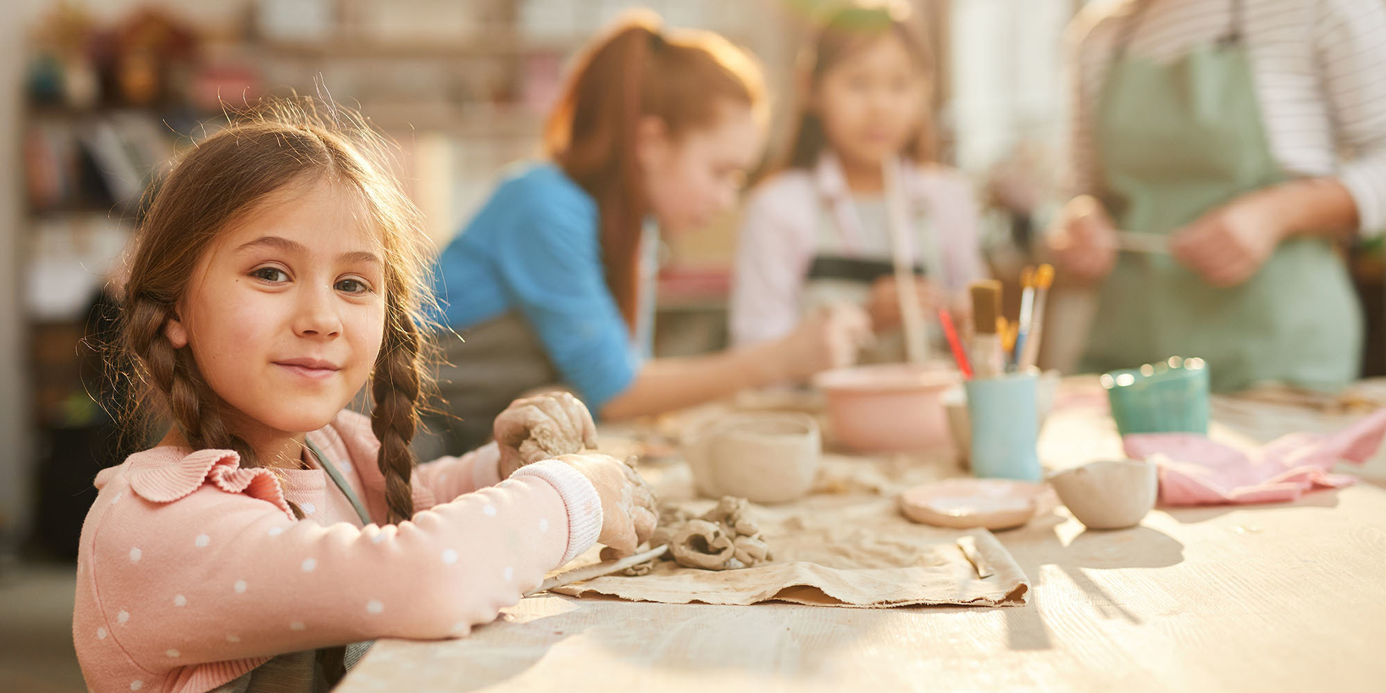 Portrait of cute little girl looking at camera while enjoying pottery class with group of children