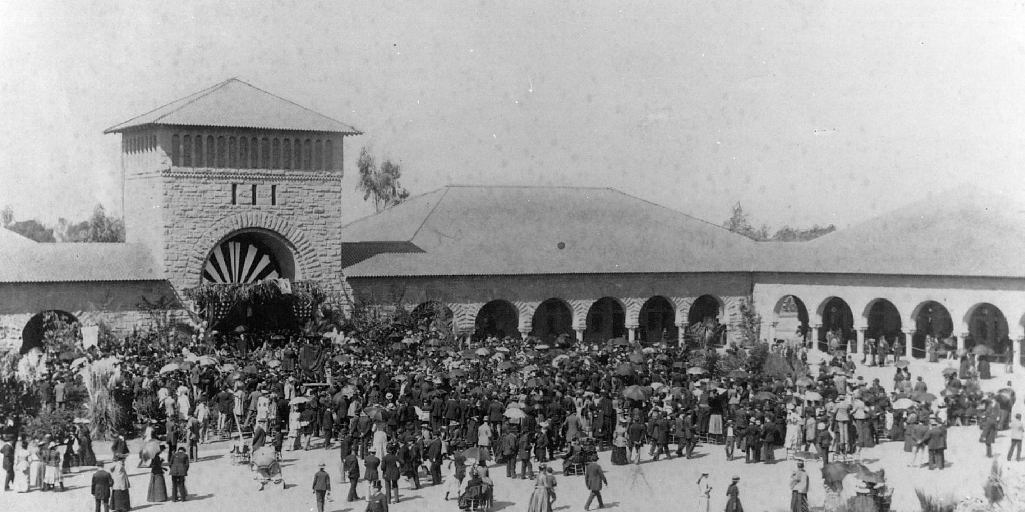 President Jordan addresses the crowd at Opening Day, Oct 1, 1891, as Leland and Jane Stanford sit beneath portrait of Leland Jr. under the large archway.