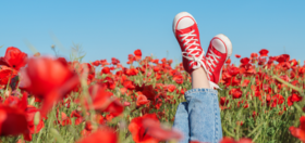 Persons legs sticking up from red flower bed and they're wearing red sneakers